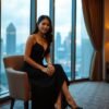 Elegant woman in black dress sits with city skyline view.